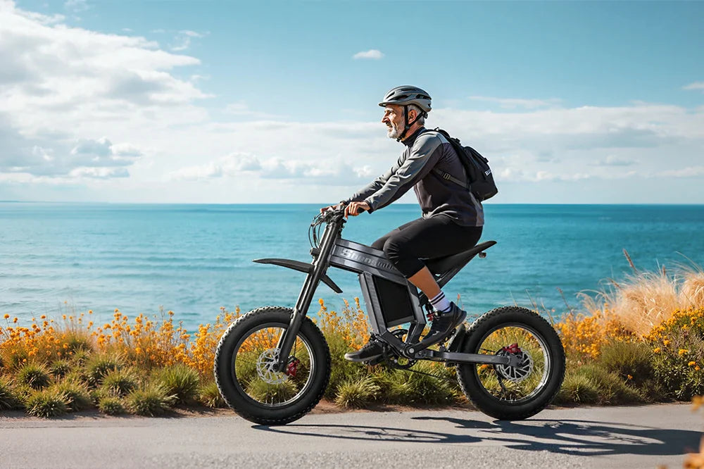 Senior man with helmet riding Shengmilo S900 rugged electric bike along coastal road with turquoise ocean and blooming flowers under bright sky