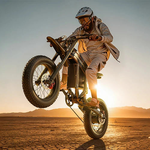 Black Shengmilo S900 high-power motorized electric off-road bike, rider in beige outfit and helmet performing wheelie trick on dry cracked desert ground, golden sunset mountain backdrop for extreme e-bike sport promotion