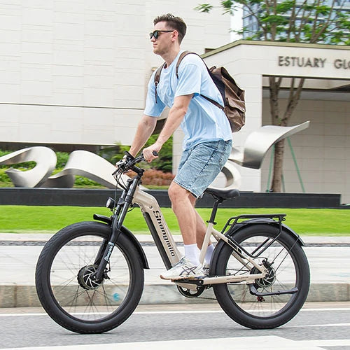 Khaki Shengmilo S700 full suspension fat tire electric bike, male rider with backpack riding on urban roadside near modern building, daily city commute outdoor photography